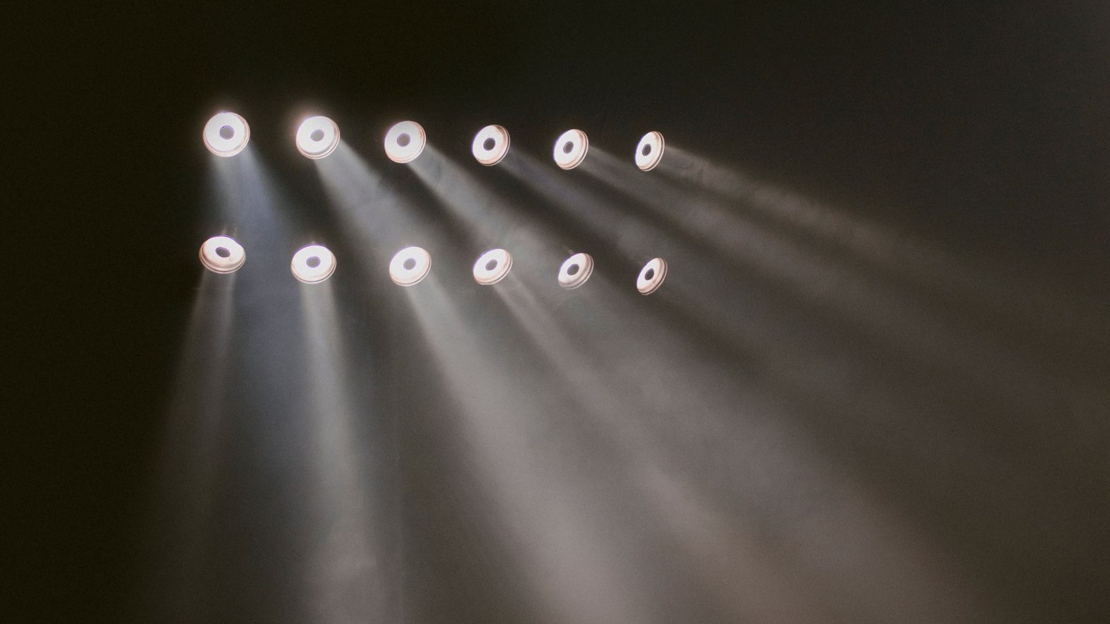 Rows of stage lighting fixtures beaming through haze